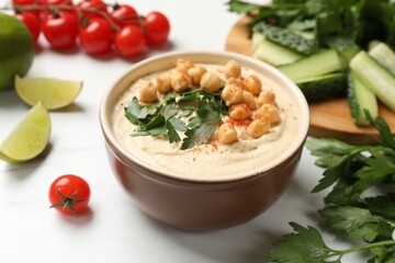 Tasty hummus with chickpeas in bowl and fresh products on light table, closeup