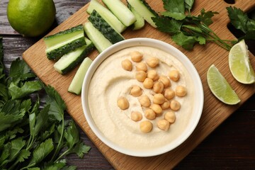 Tasty hummus with chickpeas in bowl and fresh products on wooden table, flat lay