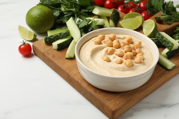 Tasty hummus with chickpeas in bowl and fresh products on light table