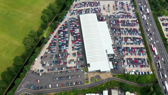 Aerial drone footage a car storage yard or car dealership showing an excess of un sold cars, taken on a hot sunny summers day next to a busy motorway