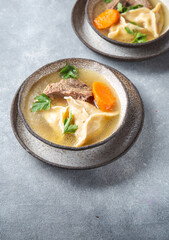 Traditional Jewish Kreplach soup with meat and carrot, gray background