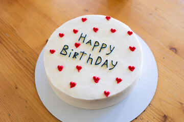 Birthday cake with the words Happy Birthday written on it, surrounded by red heart decorations.
