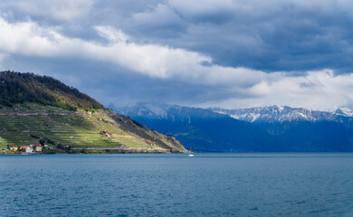 Landscape picture of a sailing boat on the Lake Leman, with the French Alps and the Lavaux Region (Switzerland) with green vineyards on a cloudy day of spring 