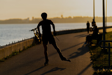 Roller skier riding roller skates in sunset next to a river in warm summer night training for...
