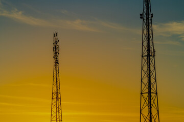 Couple of communication internet towers in the sunset of orange sky