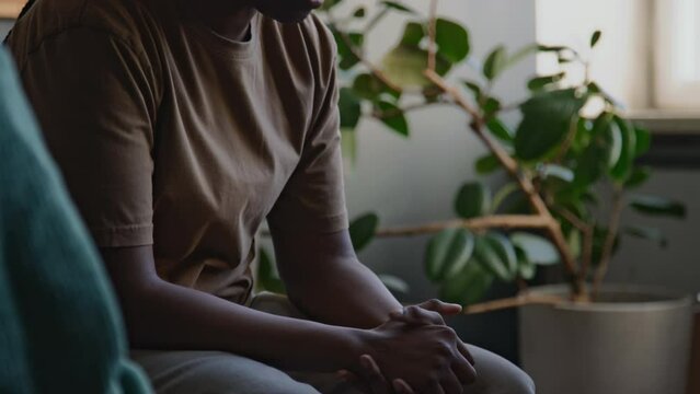 Side tilt shot of young African American woman talking about traumatic past events and finding it hard to explain her feelings during ptsd therapy session in modern psychological center