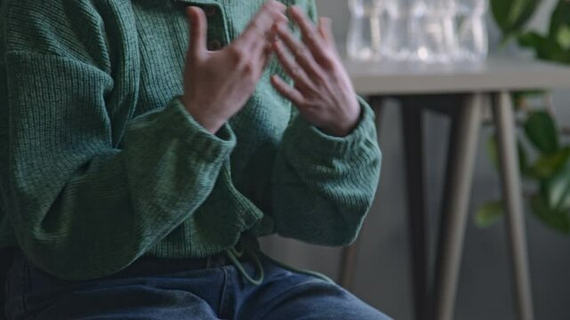 Cropped side shot of gesticulating hands of anonymous woman in green hoodie and jeans sharing her psychological problems with offscreen therapist during therapy session indoors