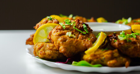 A plate of fried food with a white sauce and lemon wedges