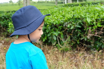 A young boy in a blue shirt and navy hat glances to the side while standing in a lush, green environment. His curious expression makes this image perfect for themes of exploration, adventure, and natu