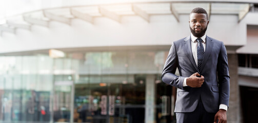 Portrait of confident african american businessman in a stylish suit standing against office building looking at camera, copy space