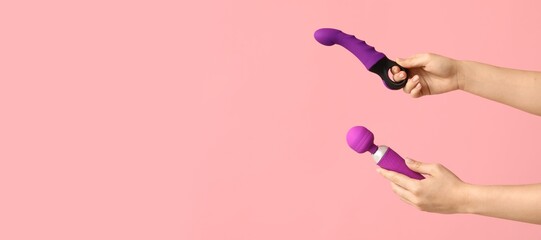 Hands of young woman holding sex toys on pink background with space for text