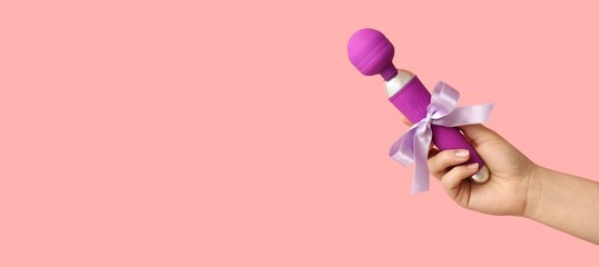 Hand of young woman holding vibrator on pink background with space for text