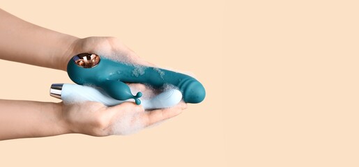 Hands of woman washing vibrators on beige background