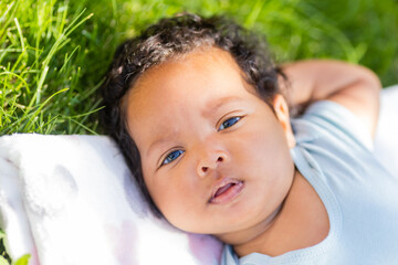 baby African-American girl in a bodysuit lies on the lawn in summer