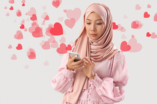 Beautiful young Asian woman in hijab with mobile phone on grey background - Powered by Adobe