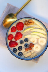 Bowl filled with healthy smoothie, fruit pieces and nuts on the table. Flat lay.