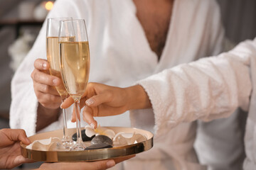 Young couple taking glasses of champagne in spa salon, closeup