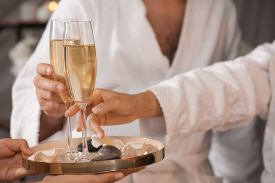 Young couple taking glasses of champagne in spa salon, closeup