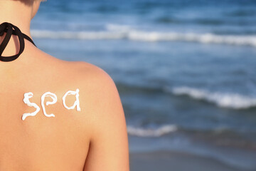Fototapeta premium Sun protection and skincare at the beach, word sea written with sunscreen on a woman's back