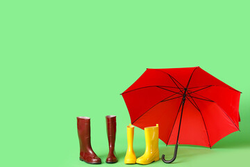 Red stylish umbrella and different gumboots on green background