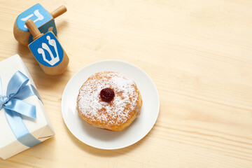 Plate with tasty donut, dreidels and gift for Hanukkah celebration on wooden background