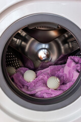 Three white wash balls and purple towel in washing machine tub. Eco-friendly household concept. Vertical banner, selective focus