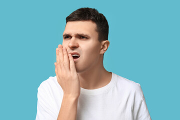Handsome young man feeling bad smell from mouth on blue background