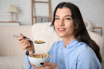 Young woman with bowl of tasty cereal rings at home, closeup