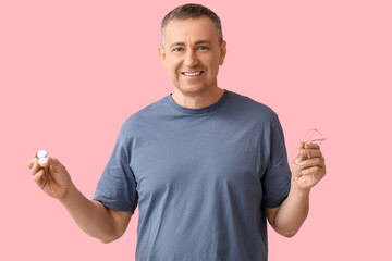 Happy mature man with contact lens case and eyeglasses on pink background