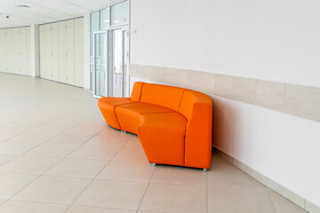 Modern public building interior featuring bright orange modular sofa against white tiled wall....