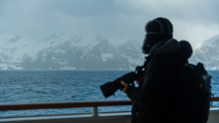 Obraz premium Antarctica Cruise Male Professional Photographer With Telephoto Lens Soft Focus Sharp On Distance Mountains Incredible Landscape Over Hand Rail