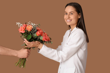 Young woman receiving bouquet of beautiful flowers on brown background