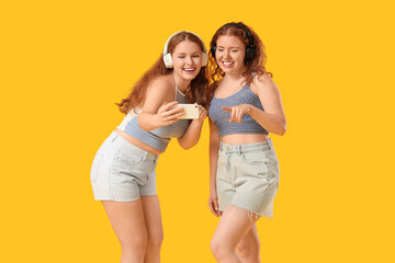 Happy redhead sisters in headphones taking selfie on yellow background