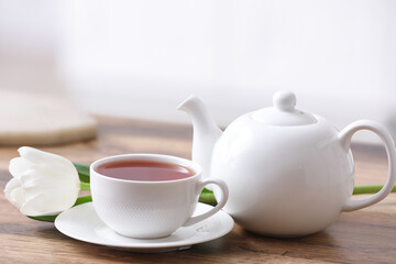 Hot cup of tea, pot and tulip on table against blurred background