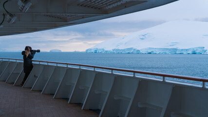 Epic Wide View Female Photographer on Antarctica Cruise Ship Promenade Deck Aims Professional Camera at Icebergs and Glaciers Neumayer Channel © And They Travel