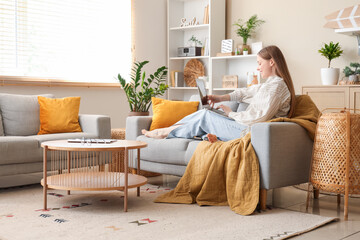Beautiful young woman using laptop and relaxing on sofa in living room