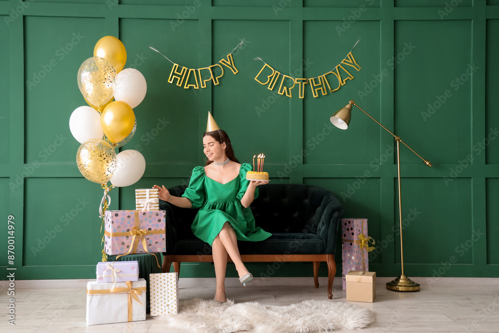 Sticker Young woman in party hat with Birthday cake and gifts sitting on sofa near green wall