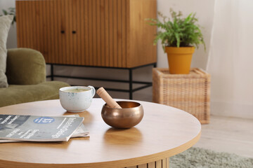 Tibetan singing bowl with cup and magazines on table in living room, closeup