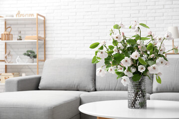 Stylish living room with grey sofa, coffee table and bouquet of blooming tree branches