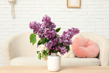 Vase with lilacs branches on table near sofa in light living room