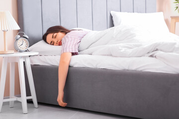 Pretty young woman sleeping in bed with alarm clock on bedside table