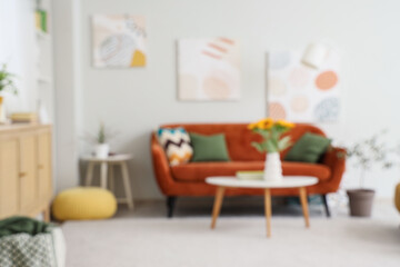Fototapeta premium Comfortable sofa and sunflower in vase on table in living room, blurred view