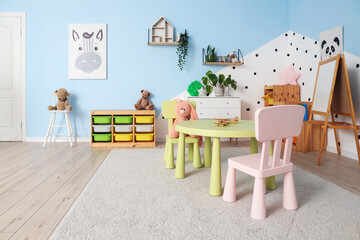 Interior of modern playroom in kindergarten with chest of drawers, shelving unit and table with chairs