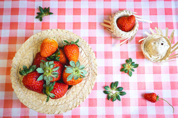 Fresh strawberries decorated on a straw hat. on a red picnic blanket.