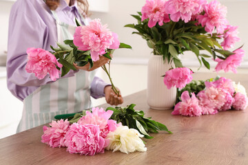 Young woman cutting peony flowers at table in kitchen
