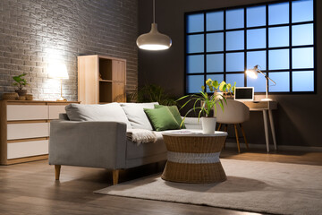 Interior of living room with comfortable sofa, tables and glowing lamps