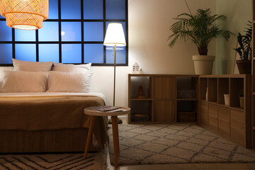 Interior of bedroom with comfortable bed, rack and glowing lamps