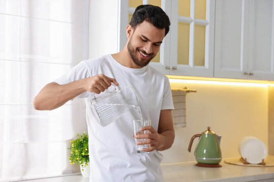 Morning of happy man pouring water from jug into glass in kitchen - Powered by Adobe