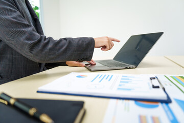 A businesswoman in a grey suit works from home, specializing in policy and planning analysis, managing financial tasks at desk with a whiteboard and expertise in accounting and financial services.