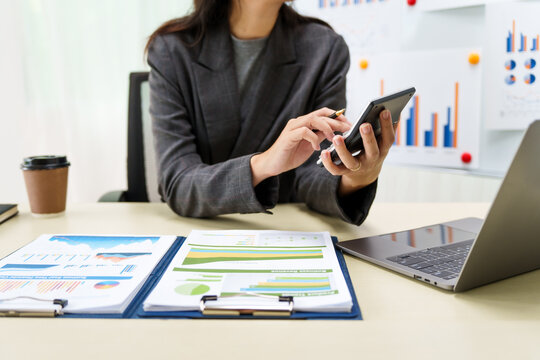 A businesswoman in a grey suit works from home, specializing in policy and planning analysis, managing financial tasks at desk with a whiteboard and expertise in accounting and financial services.